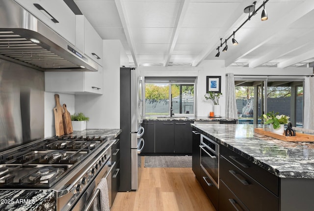 5809 N 10th Pl, Phoenix, AZ 85014 - kitchen featuring under cabinet range hood, beamed ceiling, white cabinetry, stainless steel appliances, and light wood-style flooring