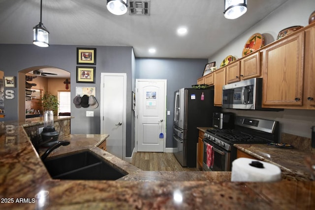 kitchen with sink, light hardwood / wood-style flooring, dark stone countertops, hanging light fixtures, and stainless steel appliances