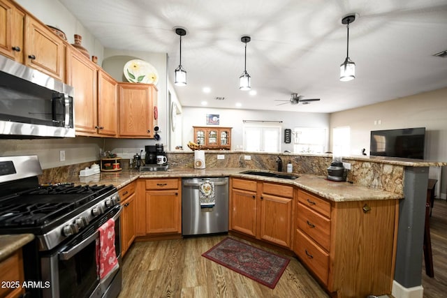 kitchen with sink, hanging light fixtures, kitchen peninsula, and appliances with stainless steel finishes