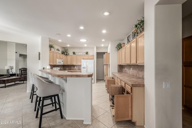 kitchen with a kitchen bar, backsplash, white appliances, light brown cabinets, and light tile patterned floors