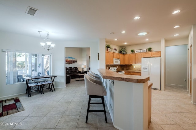 kitchen featuring white appliances, hanging light fixtures, decorative backsplash, light tile patterned floors, and a kitchen bar