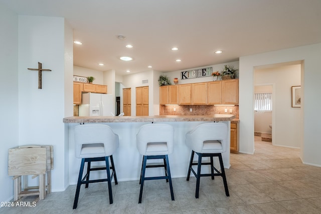 kitchen featuring backsplash, white fridge with ice dispenser, light brown cabinetry, a kitchen bar, and kitchen peninsula