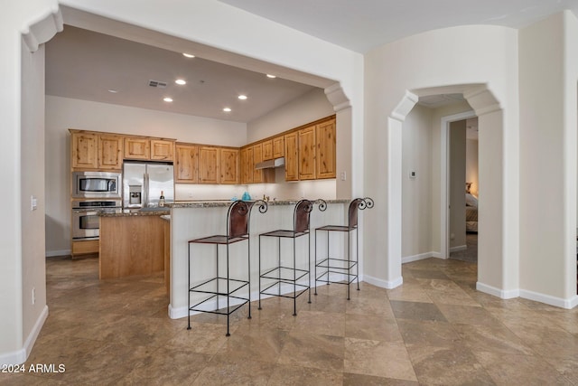 kitchen with a kitchen breakfast bar, a kitchen island, stainless steel appliances, and dark stone counters