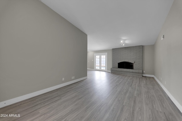 unfurnished living room featuring french doors, light hardwood / wood-style floors, and a brick fireplace