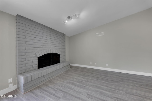 unfurnished living room featuring a brick fireplace, lofted ceiling, and light wood-type flooring