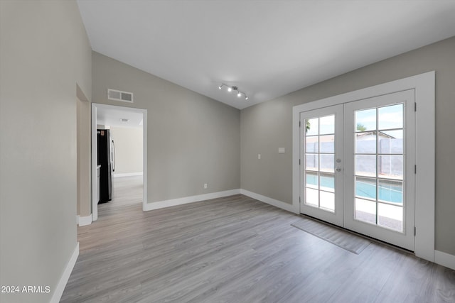 empty room featuring french doors, vaulted ceiling, and light wood-type flooring