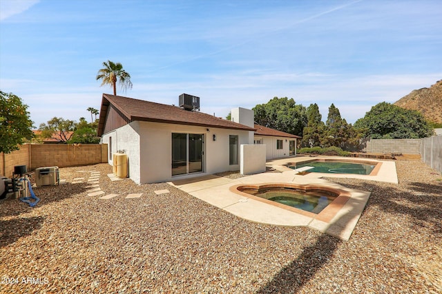 rear view of property featuring a swimming pool with hot tub, central AC unit, and a patio