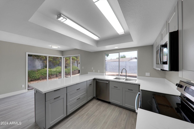 kitchen featuring sink, light wood-type flooring, appliances with stainless steel finishes, kitchen peninsula, and a raised ceiling