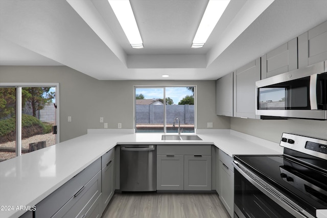 kitchen featuring gray cabinets, appliances with stainless steel finishes, sink, kitchen peninsula, and a raised ceiling