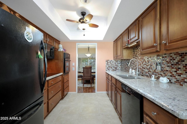 kitchen featuring a tray ceiling, backsplash, brown cabinetry, a sink, and black appliances