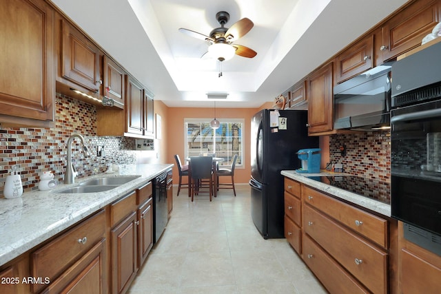 kitchen with black appliances, a tray ceiling, a sink, and brown cabinets