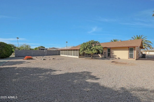 rear view of house with central AC unit, a sunroom, and fence