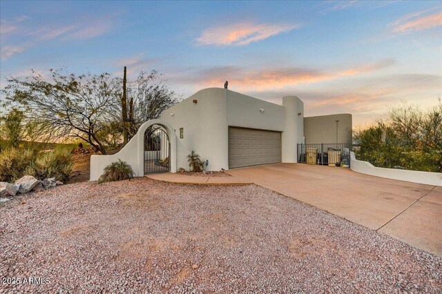 pueblo revival-style home with stucco siding, concrete driveway, a gate, fence, and a garage