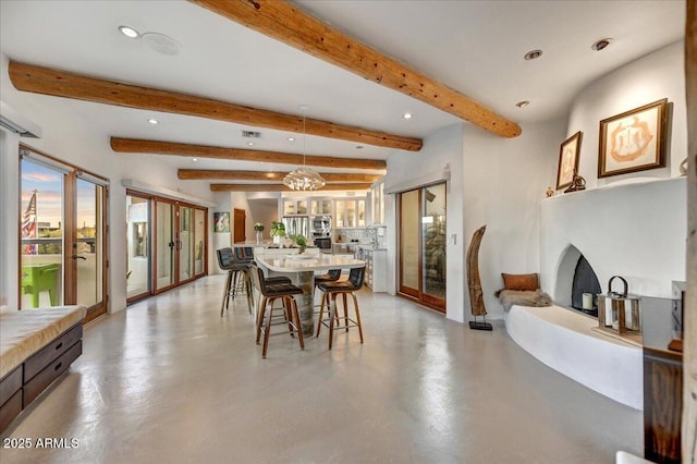 dining space with finished concrete flooring, a fireplace with raised hearth, beam ceiling, and recessed lighting