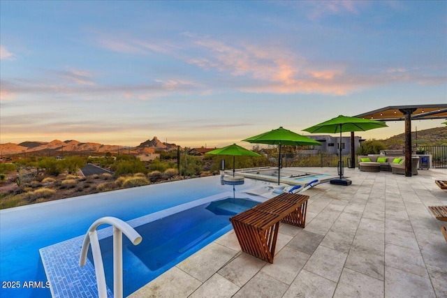 pool at dusk featuring an infinity pool, outdoor lounge area, a patio area, and fence