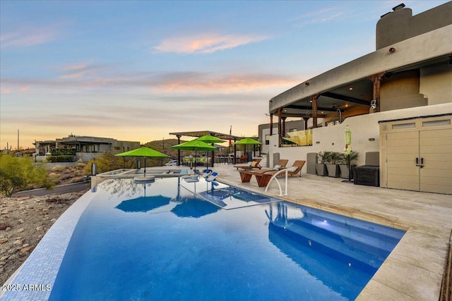 pool at dusk with a patio area and an outdoor pool