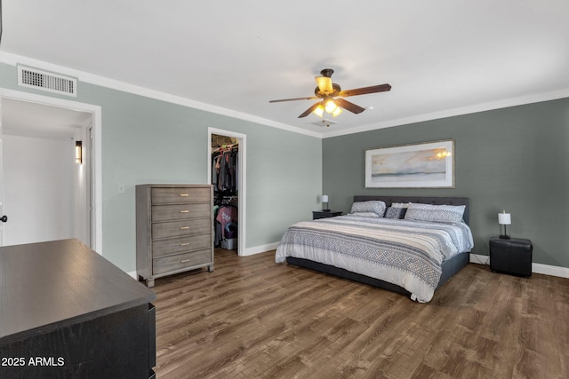 bedroom featuring wood finished floors, baseboards, a closet, a spacious closet, and ornamental molding