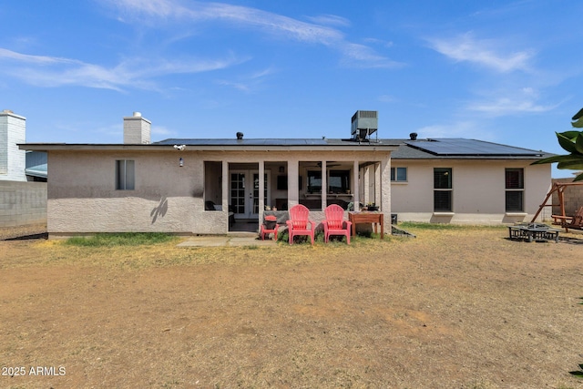 rear view of property with french doors, a fire pit, solar panels, stucco siding, and central air condition unit