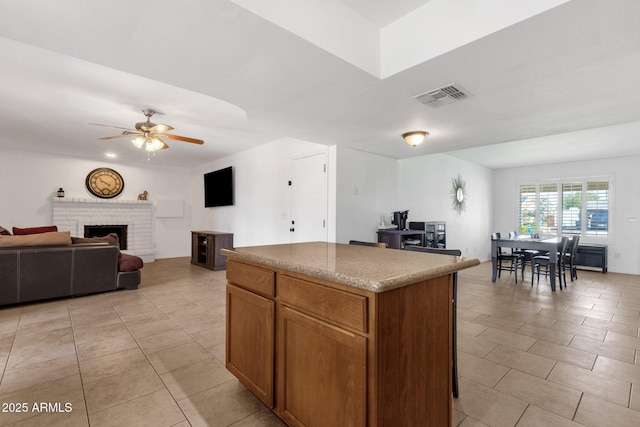kitchen with ceiling fan, a kitchen island, open floor plan, a brick fireplace, and light tile patterned floors
