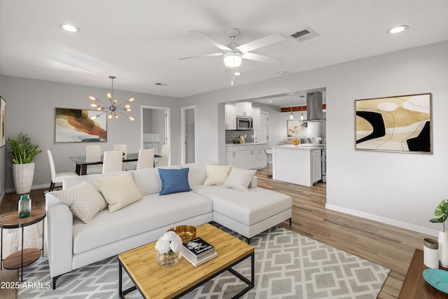 living room with ceiling fan with notable chandelier and light wood-type flooring