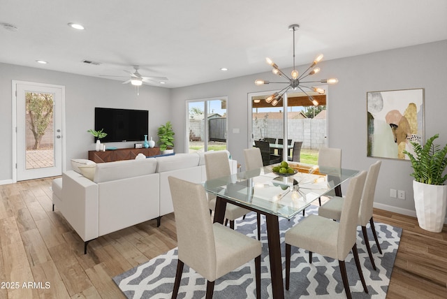 dining area with ceiling fan with notable chandelier, light hardwood / wood-style floors, and a wealth of natural light