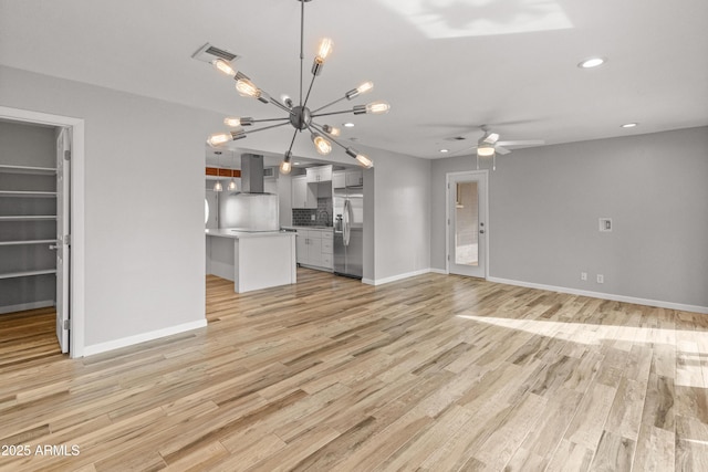 unfurnished living room with ceiling fan with notable chandelier and light wood-type flooring