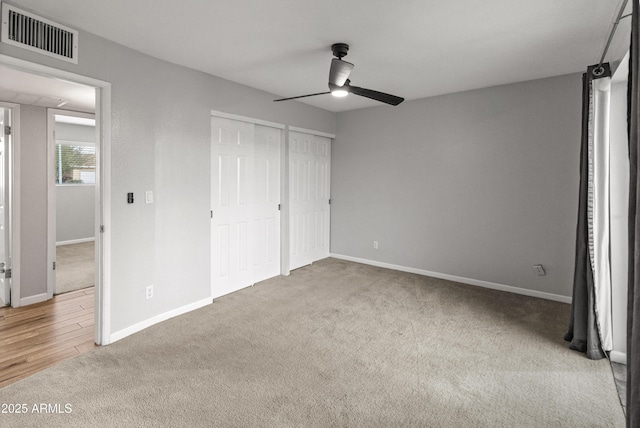 unfurnished bedroom featuring carpet, ceiling fan, and multiple closets