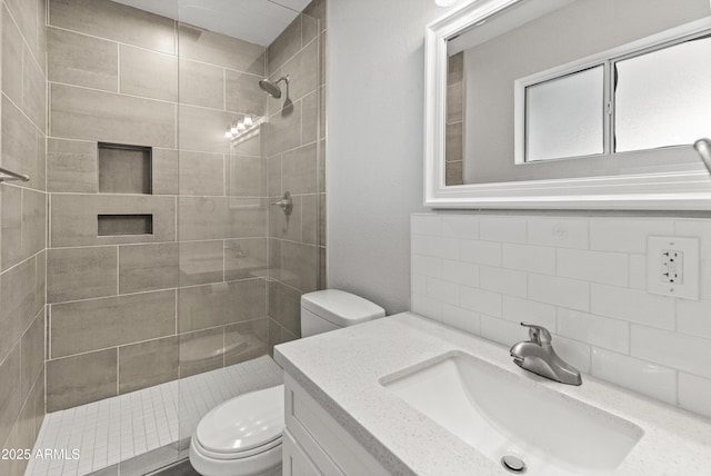 bathroom featuring tiled shower, decorative backsplash, vanity, and toilet