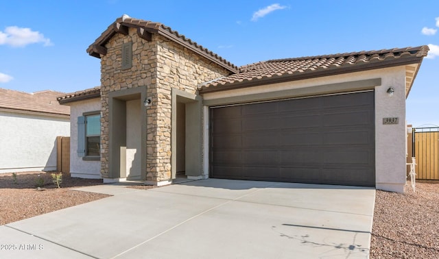 mediterranean / spanish house with a tiled roof, stucco siding, a garage, stone siding, and driveway