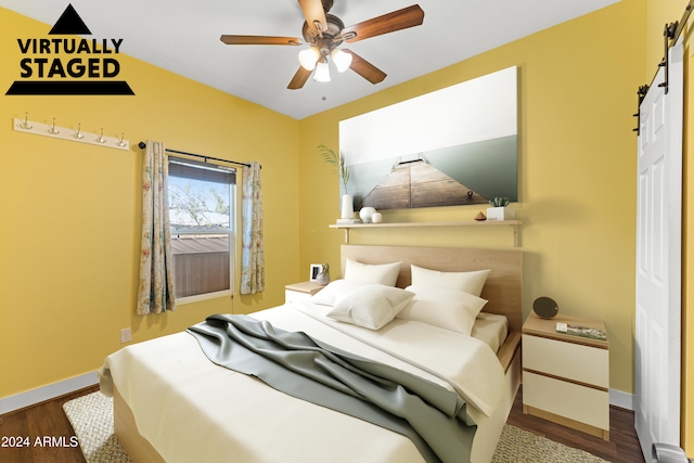 bedroom with ceiling fan, a barn door, and dark hardwood / wood-style flooring