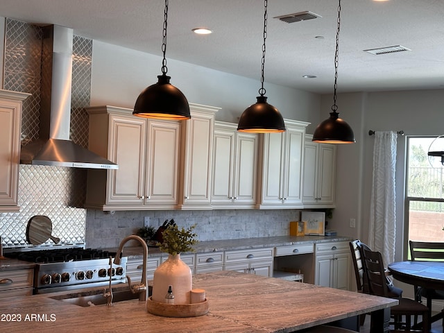 kitchen with decorative backsplash, cream cabinets, decorative light fixtures, and wall chimney range hood