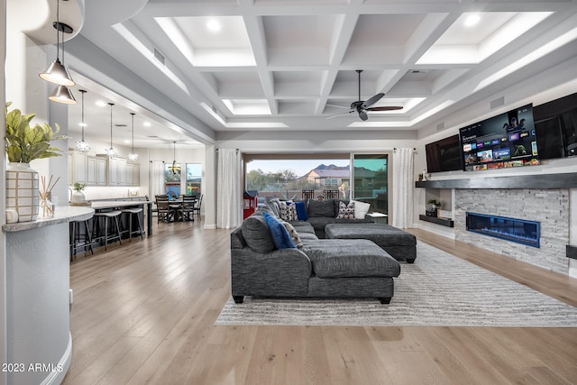 living room with coffered ceiling, light hardwood / wood-style flooring, beamed ceiling, a fireplace, and ceiling fan with notable chandelier