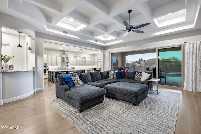 living room featuring beam ceiling, light hardwood / wood-style flooring, ceiling fan, and coffered ceiling