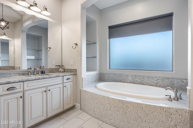 bathroom with built in shelves, vanity, a relaxing tiled tub, and a wealth of natural light