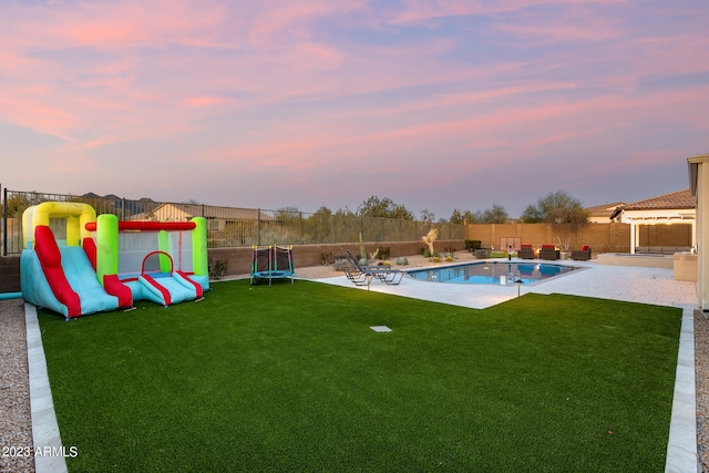 pool at dusk with a lawn, a trampoline, and a patio