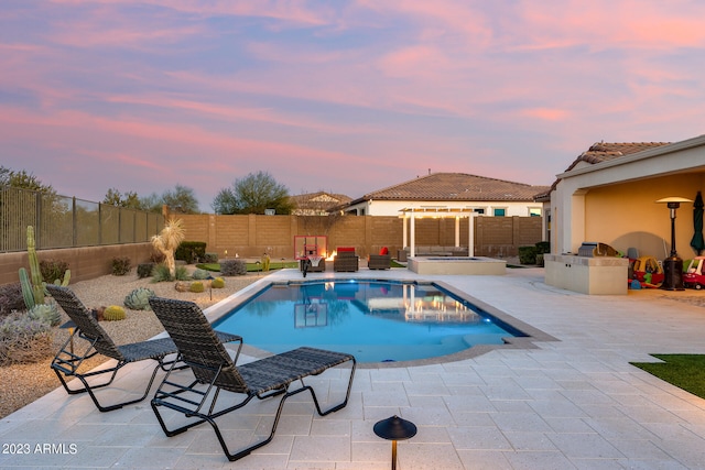 pool at dusk with a patio area and exterior kitchen