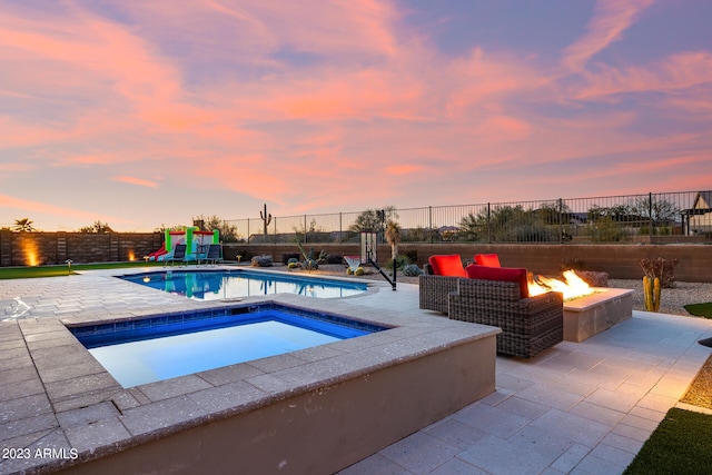 pool at dusk with an in ground hot tub, an outdoor living space with a fire pit, and a patio area