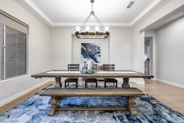 dining area with a tray ceiling, hardwood / wood-style floors, and an inviting chandelier