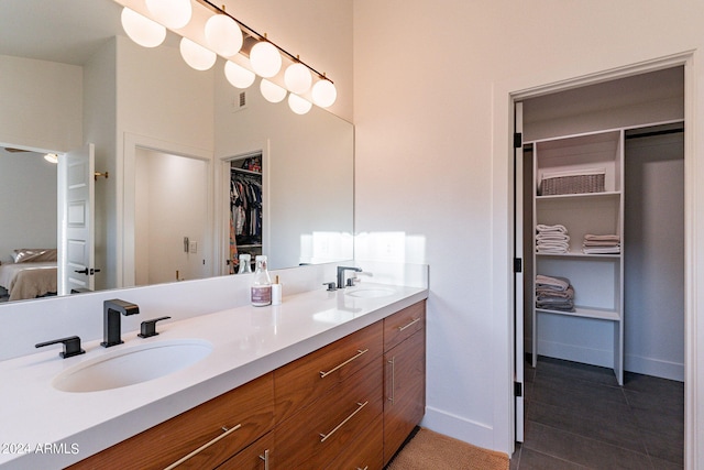 bathroom featuring double vanity, connected bathroom, a walk in closet, and a sink