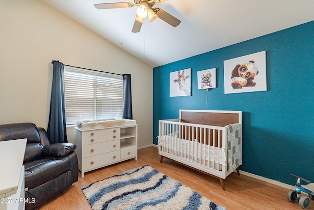 bedroom with ceiling fan, light hardwood / wood-style floors, a nursery area, and vaulted ceiling