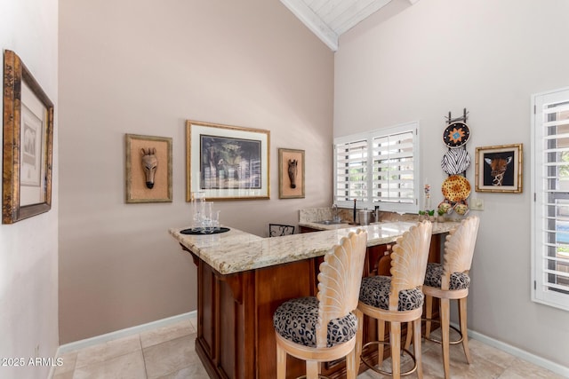 bar featuring light tile patterned floors, baseboards, high vaulted ceiling, and indoor bar