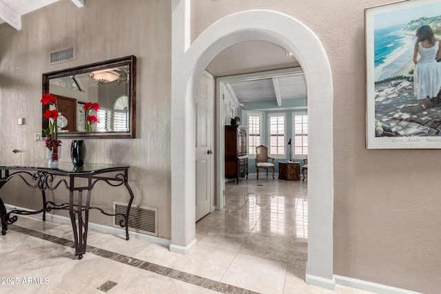 corridor featuring arched walkways, visible vents, a textured wall, and baseboards