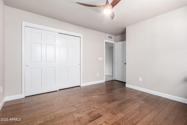 unfurnished bedroom featuring wood finished floors, visible vents, a closet, and baseboards