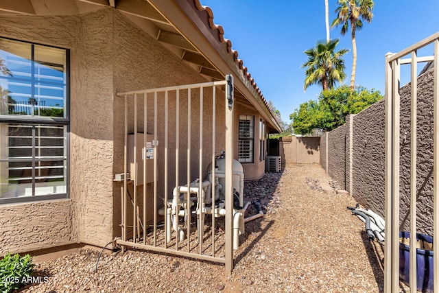 view of side of home with a tile roof, a fenced backyard, central AC, and stucco siding