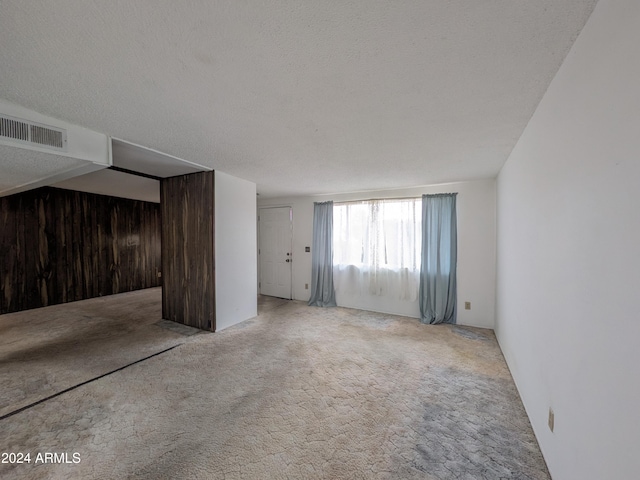 interior space with carpet floors, wood walls, visible vents, and a textured ceiling