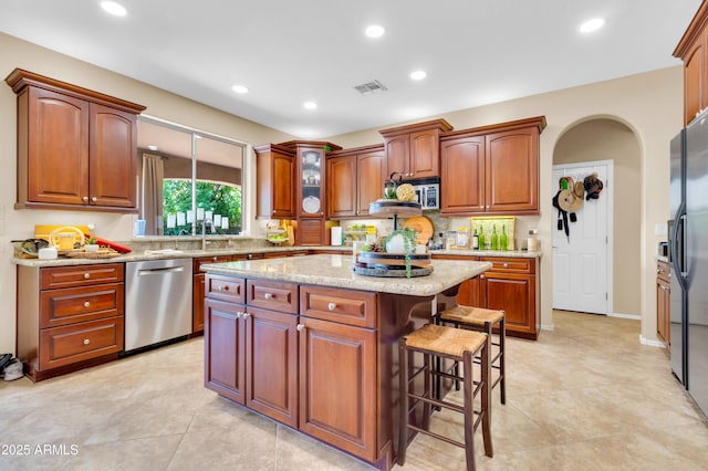 2383 E Zion Way, Chandler, AZ 85249 - kitchen with appliances with stainless steel finishes, a kitchen breakfast bar, a center island, light stone countertops, and arched walkways