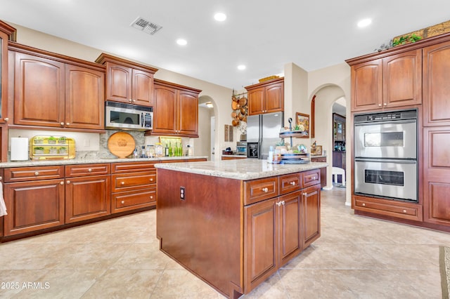 2383 E Zion Way, Chandler, AZ 85249 - kitchen featuring arched walkways, stainless steel appliances, a center island, light stone counters, and backsplash