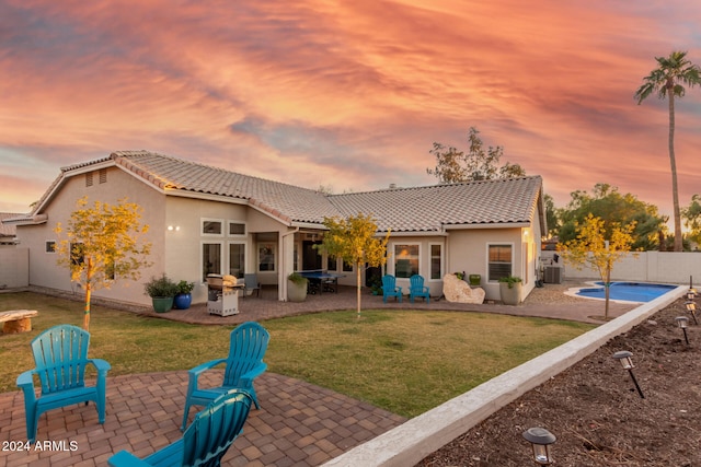 back house at dusk featuring a lawn, a patio area, a fenced in pool, and central AC