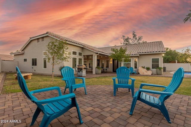 back house at dusk with a patio and a lawn