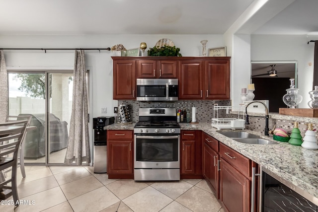 kitchen featuring light stone counters, light tile patterned flooring, a sink, appliances with stainless steel finishes, and backsplash